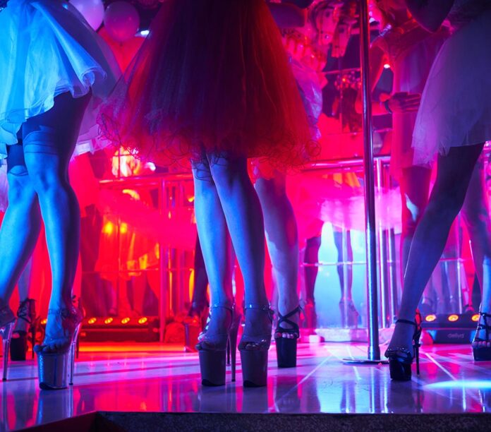 Young sexy womans pole dancing striptease in night club. Beautiful naked stripper girl on stage. Beautiful female legs in high-heeled shoes strips